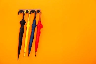 Photo of Colorful umbrellas on wooden rack in hallway, space for text