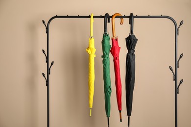 Colorful umbrellas on rack near beige wall