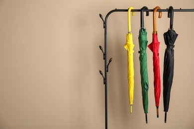 Photo of Colorful umbrellas on rack near beige wall, space for text