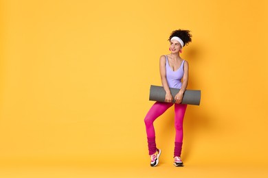 Photo of Aerobics. Woman in sportswear holding fitness mat on orange background, space for text