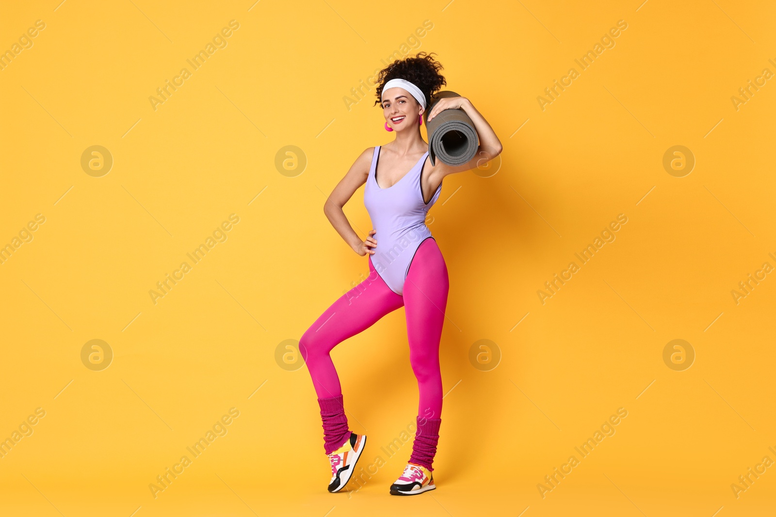 Photo of Aerobics. Woman in sportswear holding fitness mat on orange background