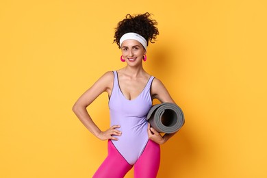 Photo of Aerobics. Woman in sportswear holding fitness mat on orange background