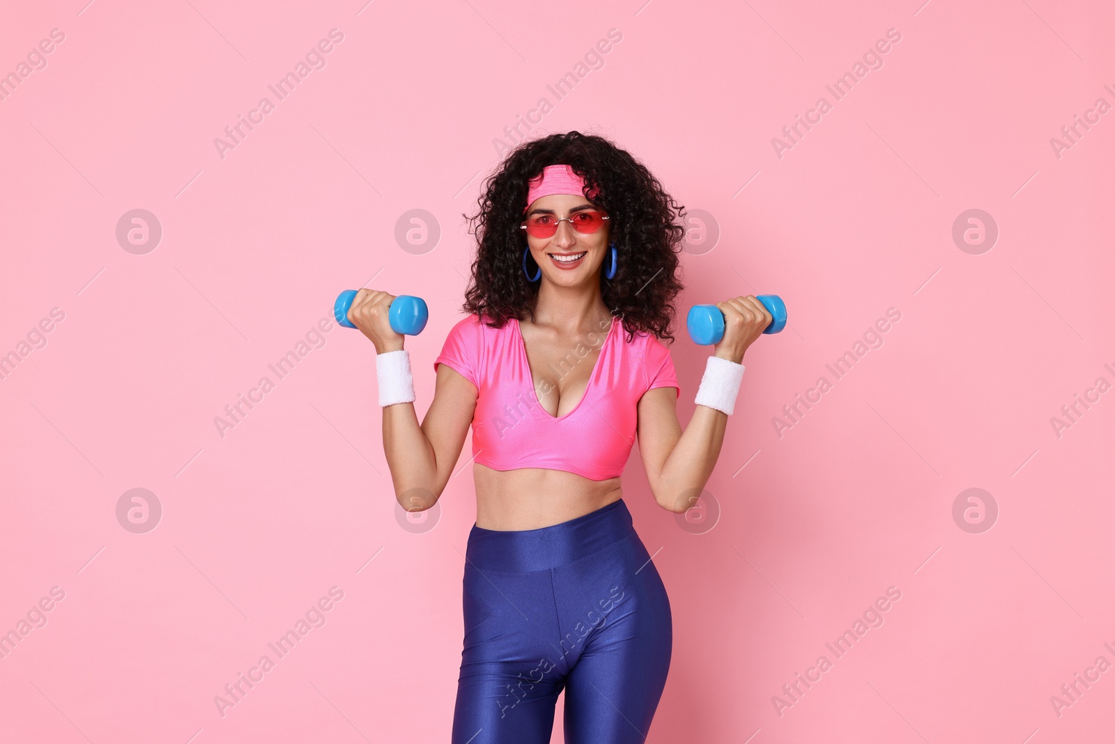 Photo of Woman doing aerobic exercise with dumbbells on pink background