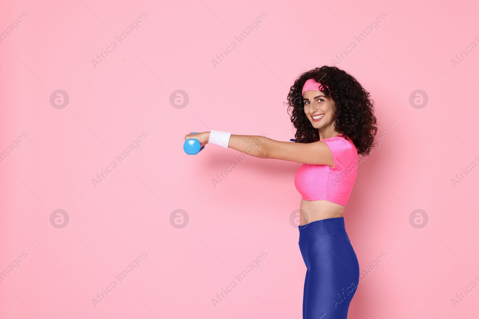 Photo of Woman doing aerobic exercise with dumbbells on pink background, space for text