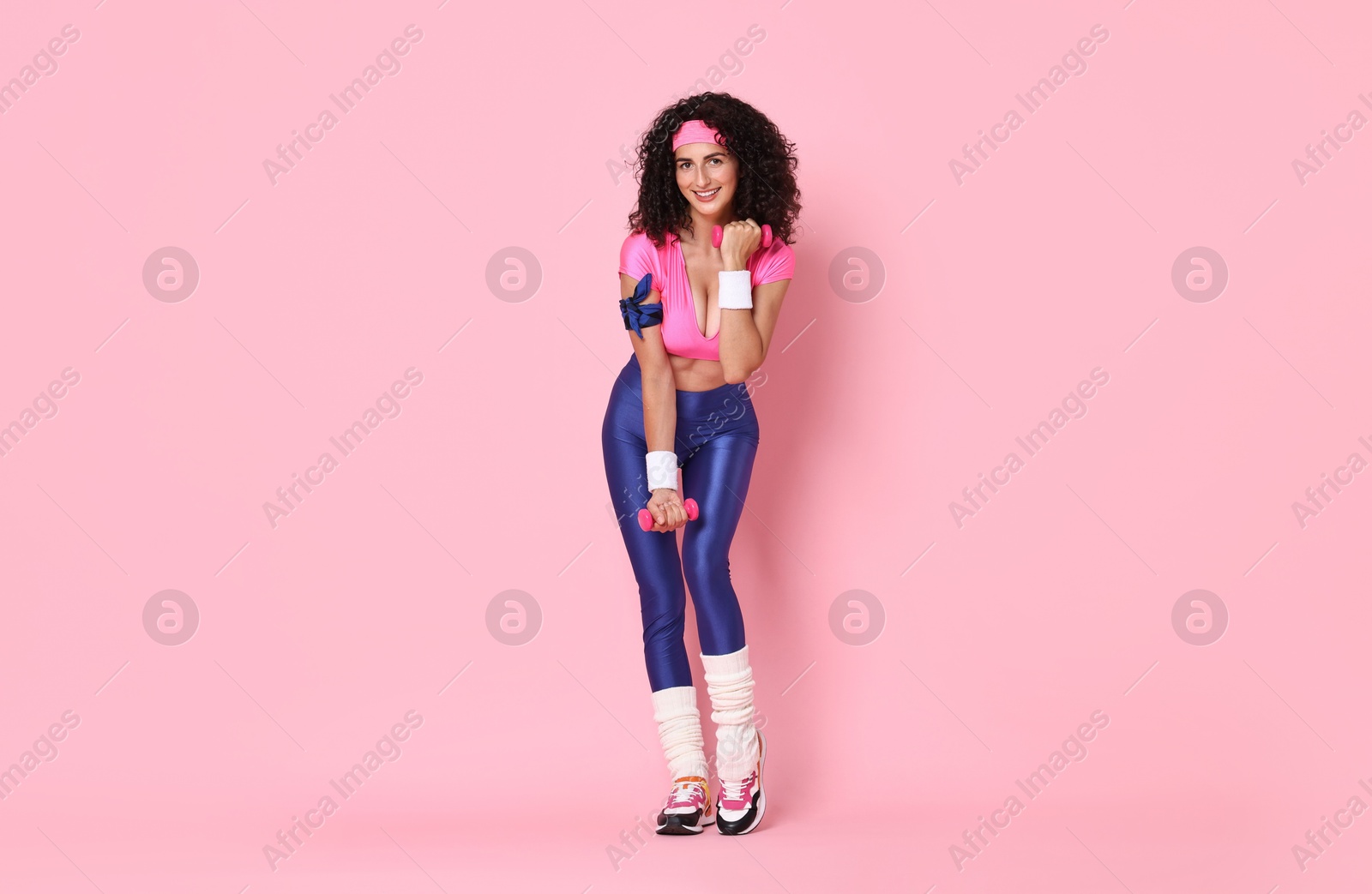 Photo of Woman doing aerobic exercise with dumbbells on pink background