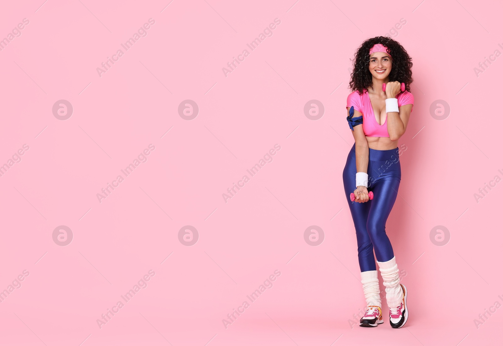 Photo of Woman doing aerobic exercise with dumbbells on pink background, space for text