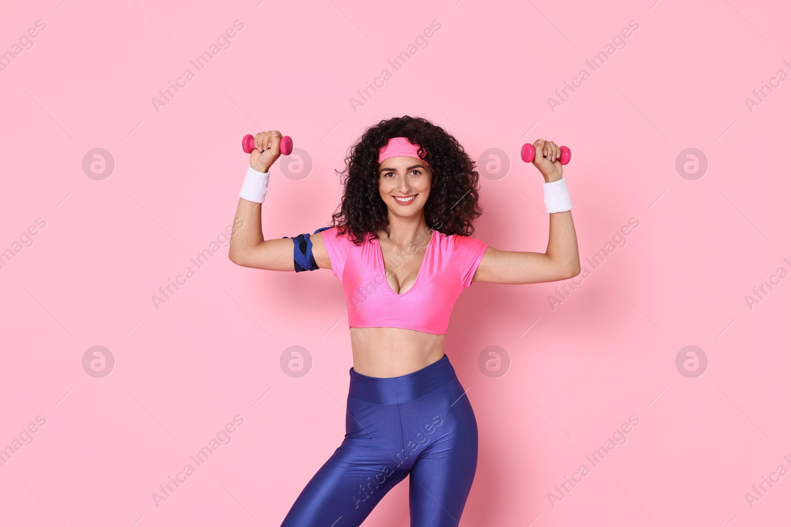 Photo of Woman doing aerobic exercise with dumbbells on pink background