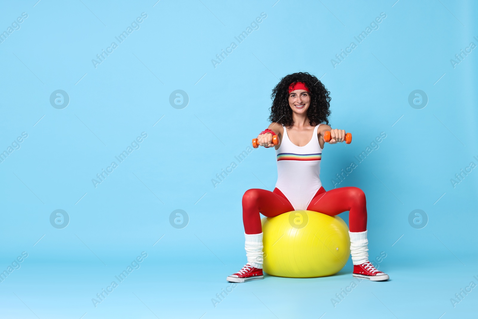 Photo of Woman doing aerobic exercise with dumbbells and fitness ball on light blue background, space for text