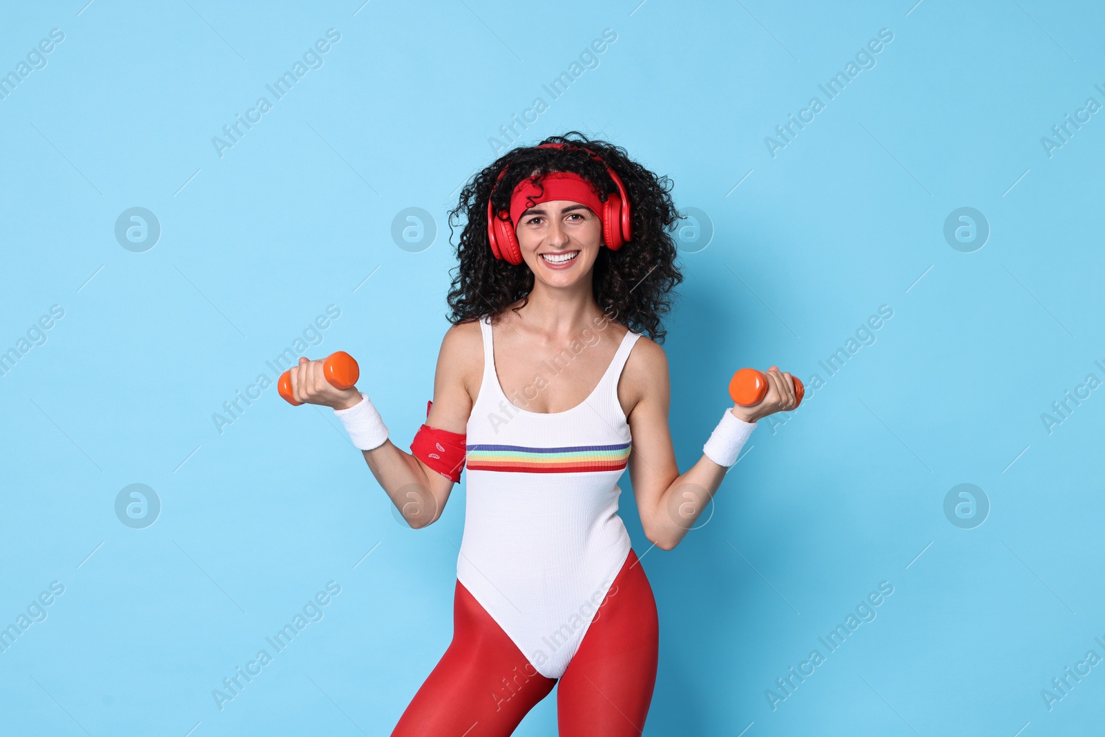 Photo of Woman in headphones doing aerobic exercise with dumbbells on light blue background