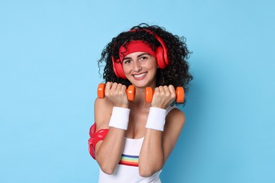 Photo of Woman in headphones doing aerobic exercise with dumbbells on light blue background