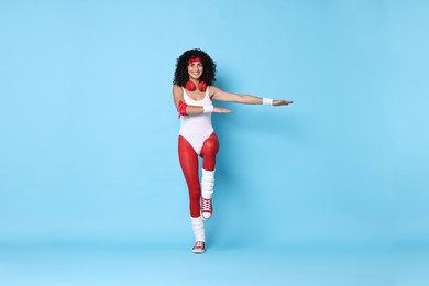 Photo of Woman with headphones doing aerobic exercise on light blue background