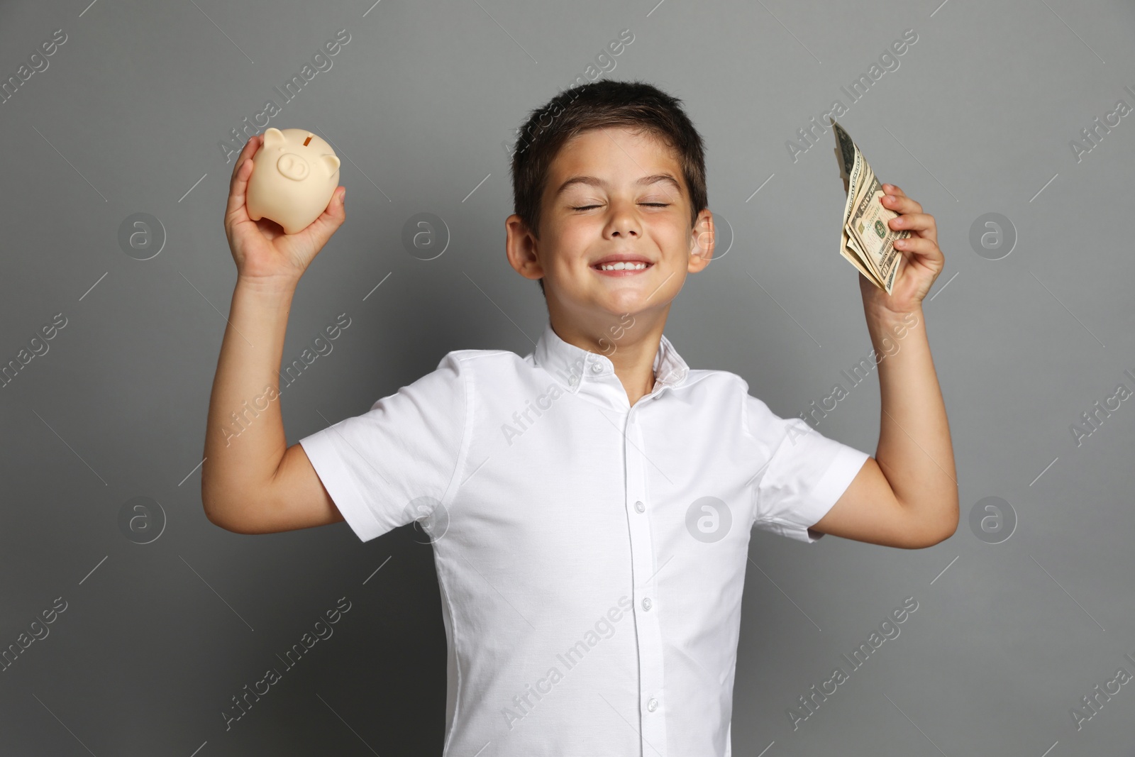 Photo of Cute boy with piggy bank and pocket money on grey background