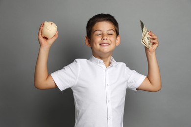 Cute boy with piggy bank and pocket money on grey background