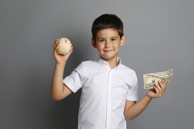 Photo of Cute boy with piggy bank and pocket money on grey background