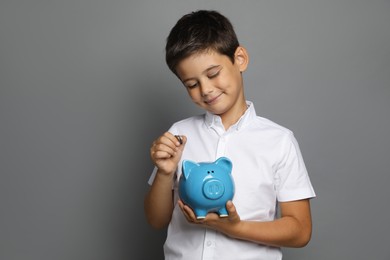 Photo of Pocket money. Cute boy with piggy bank and coins on grey background, space for text