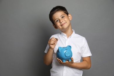 Pocket money. Cute boy with piggy bank and coins on grey background, space for text