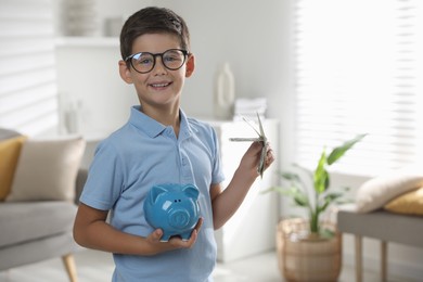 Cute boy with piggy bank and pocket money at home, space for text