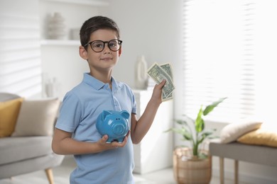 Cute boy with piggy bank and pocket money at home, space for text