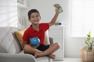 Cute boy with piggy bank and pocket money on sofa at home, space for text