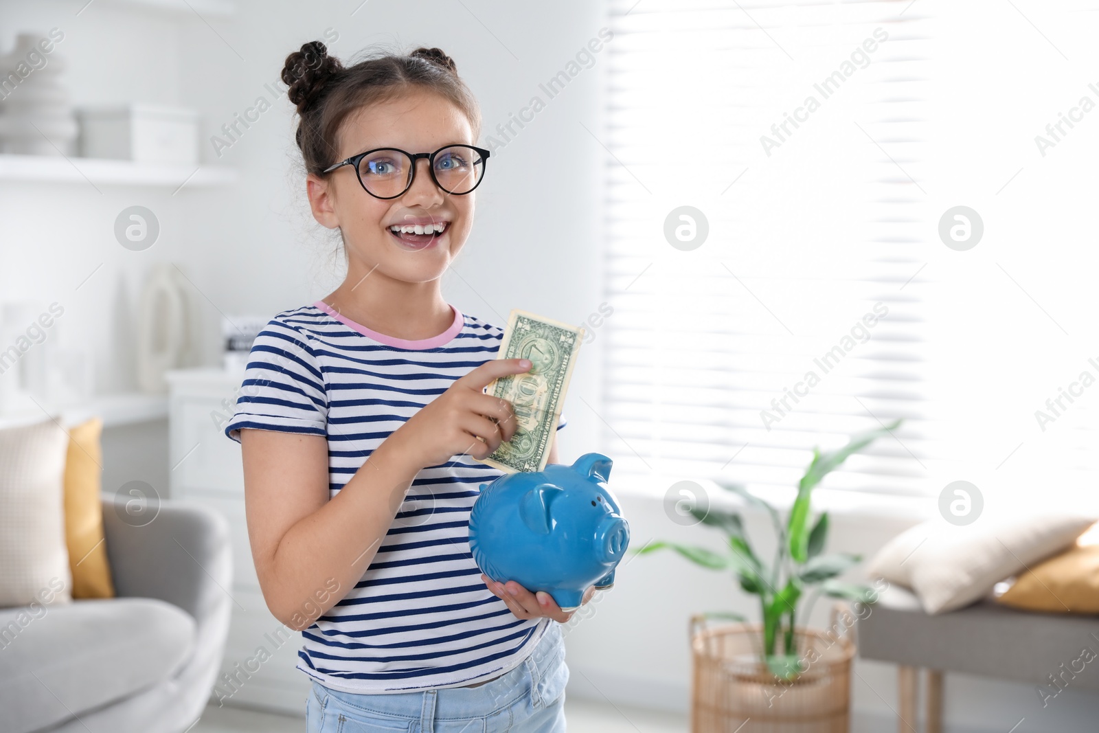 Photo of Cute girl with pocket money and piggy bank at home, space for text