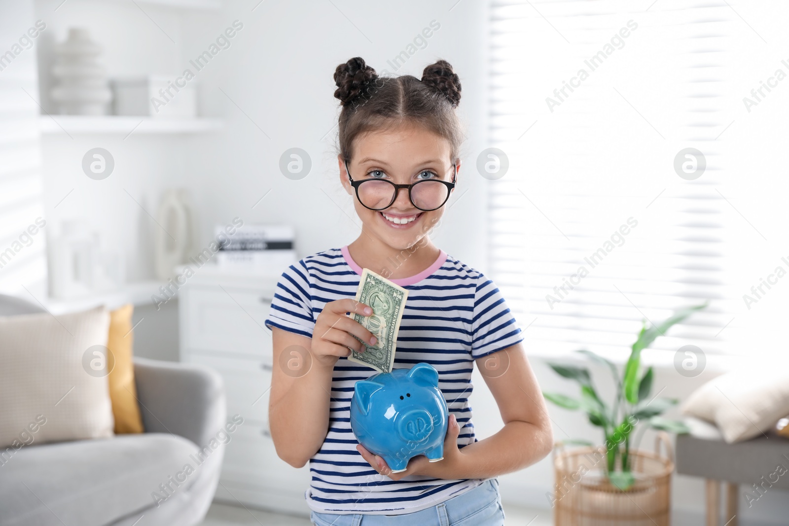 Photo of Cute girl with pocket money and piggy bank at home