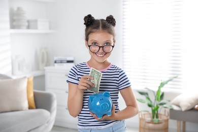 Cute girl with pocket money and piggy bank at home