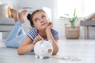 Photo of Pocket money. Cute girl putting coin into piggy bank at home, space for text