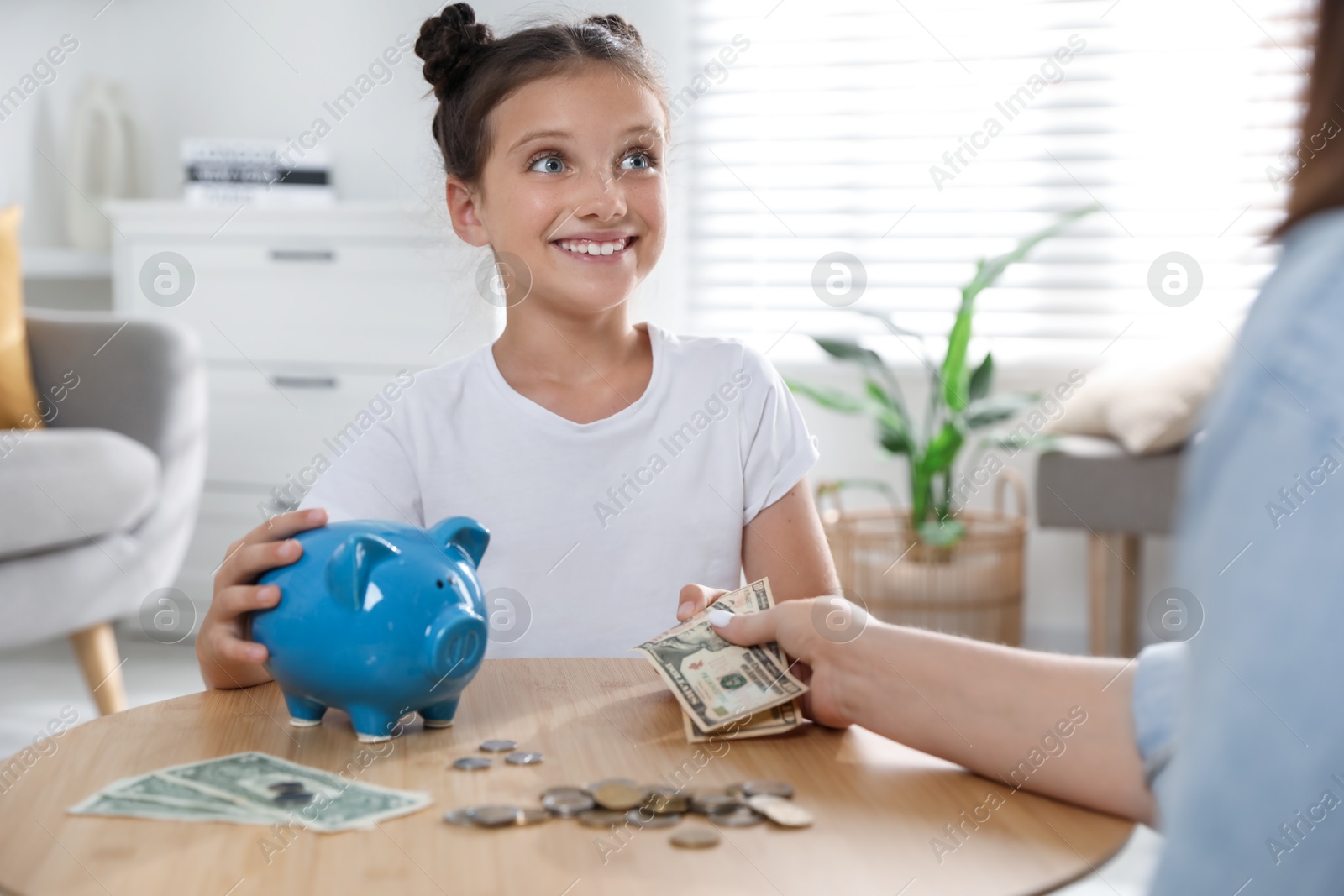 Photo of Mother giving pocket money to her daughter at table indoors