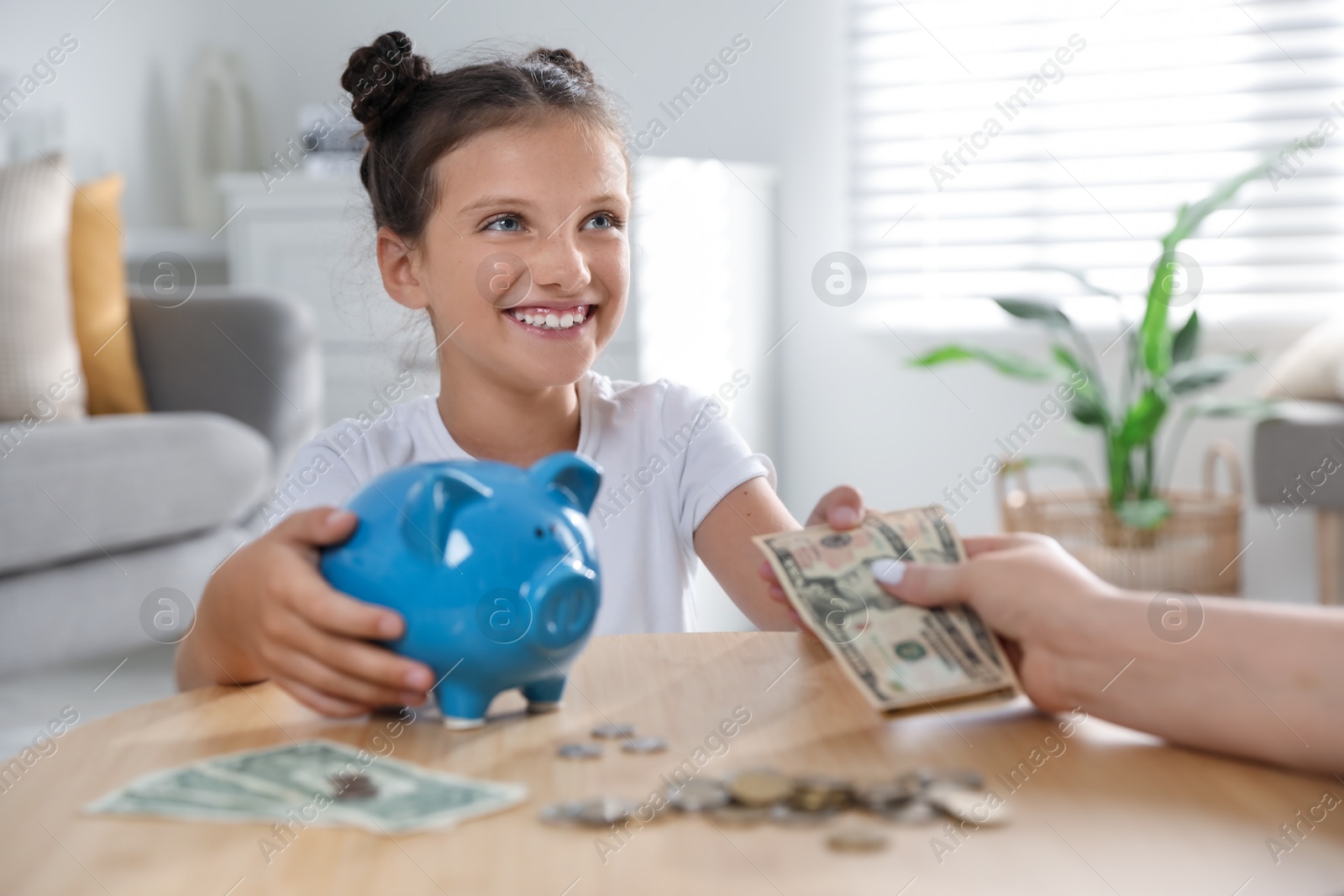 Photo of Mother giving pocket money to her daughter at table indoors