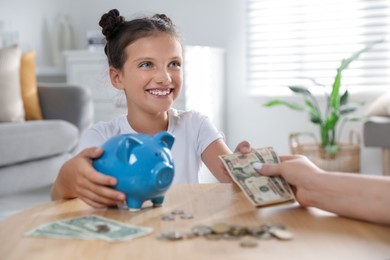 Photo of Mother giving pocket money to her daughter at table indoors