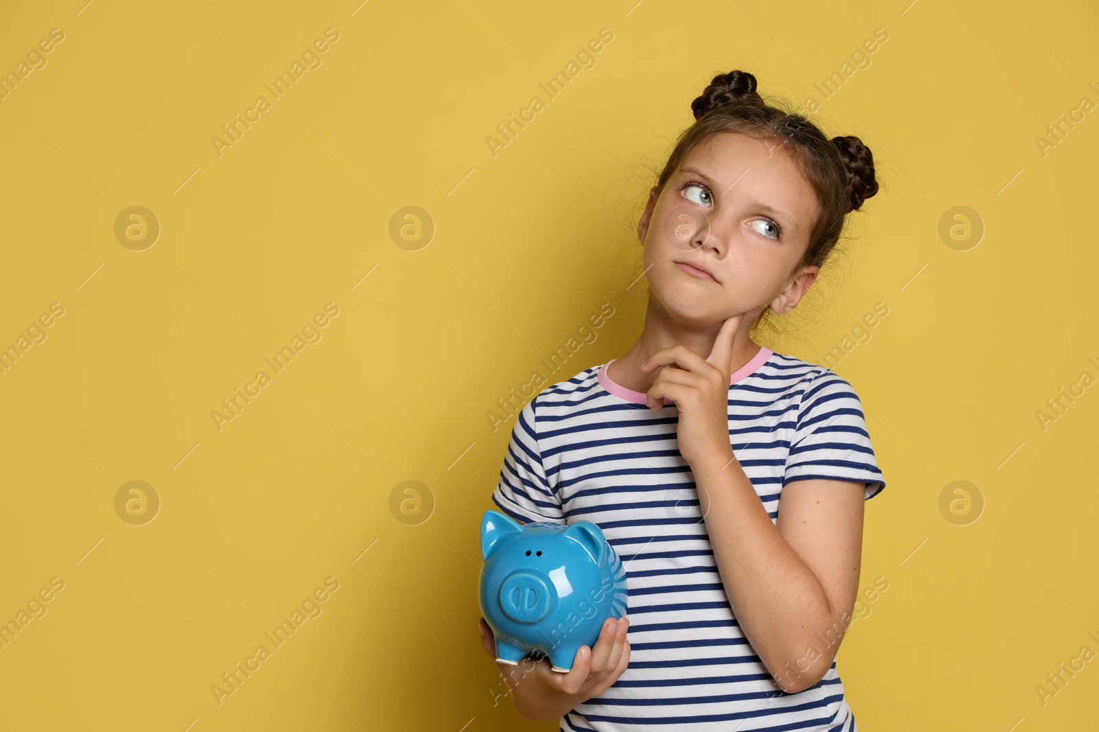 Photo of Pocket money. Cute girl with piggy bank on yellow background, space for text