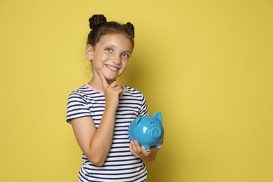 Photo of Pocket money. Cute girl with piggy bank on yellow background