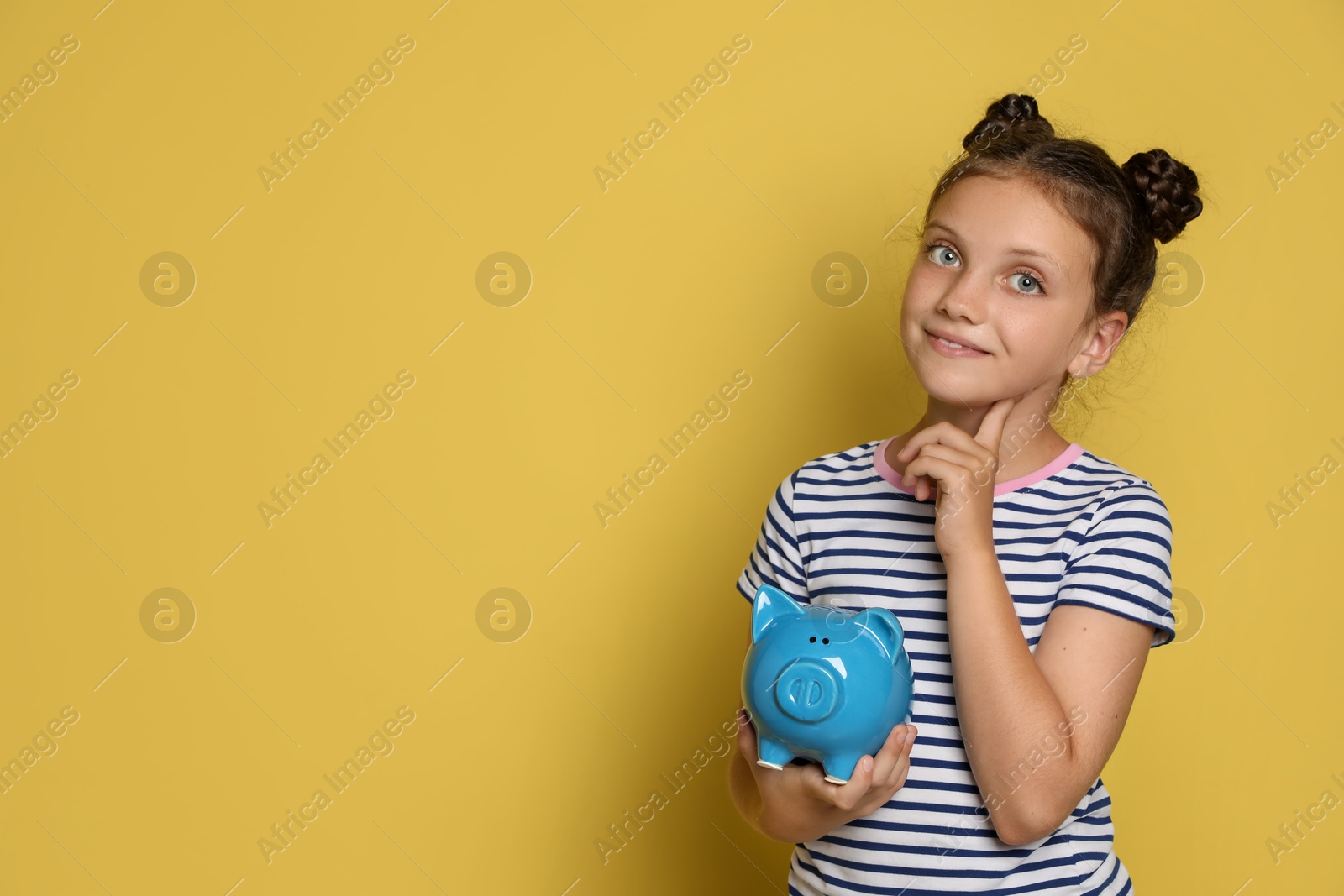 Photo of Pocket money. Cute girl with piggy bank on yellow background, space for text