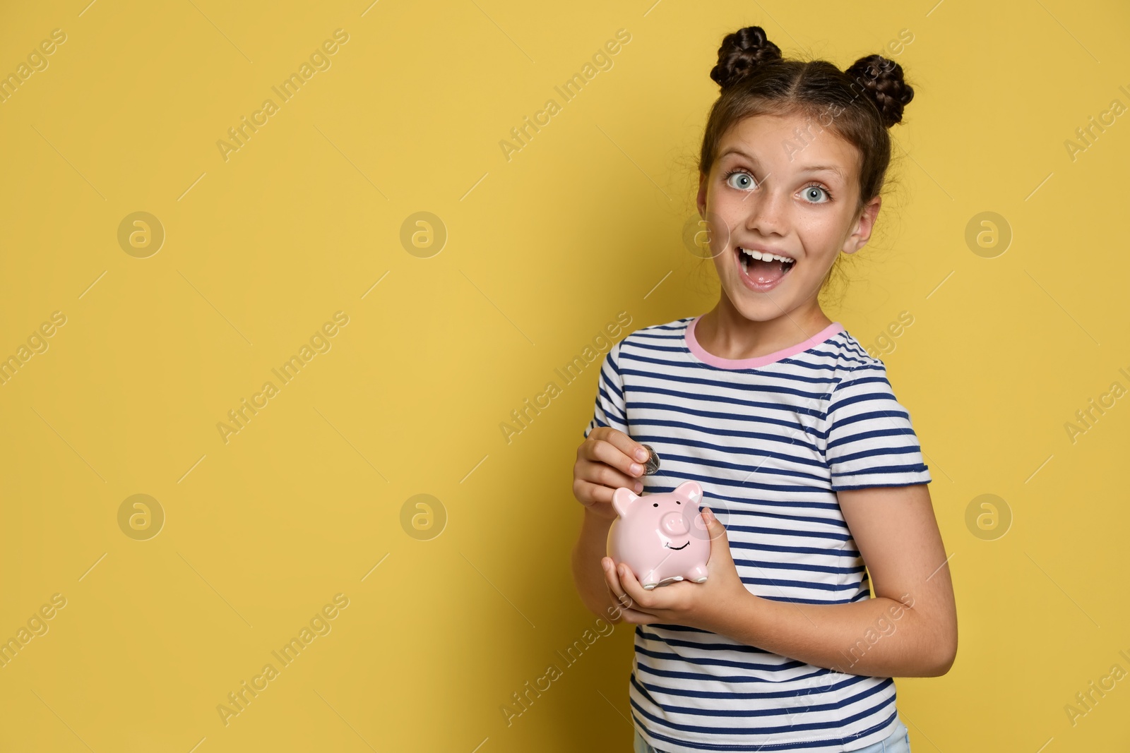 Photo of Pocket money. Cute girl putting coin into piggy bank on yellow background, space for text