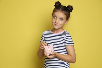 Photo of Pocket money. Cute girl putting coin into piggy bank on yellow background