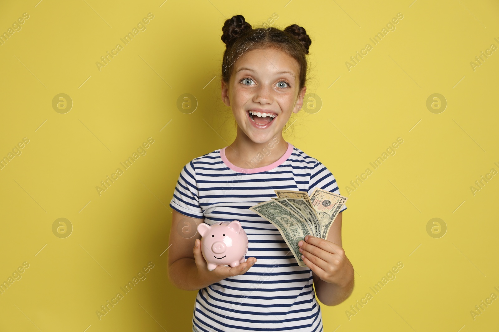 Photo of Pocket money. Cute girl with piggy bank and dollar banknotes on yellow background