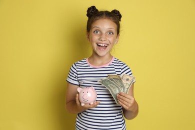 Photo of Pocket money. Cute girl with piggy bank and dollar banknotes on yellow background