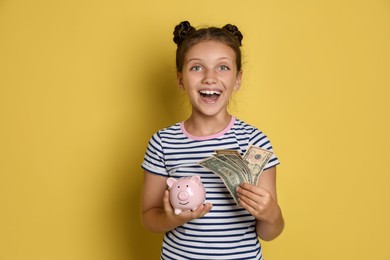 Pocket money. Cute girl with piggy bank and dollar banknotes on yellow background