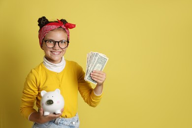 Photo of Pocket money. Cute girl with piggy bank and dollar banknotes on yellow background, space for text