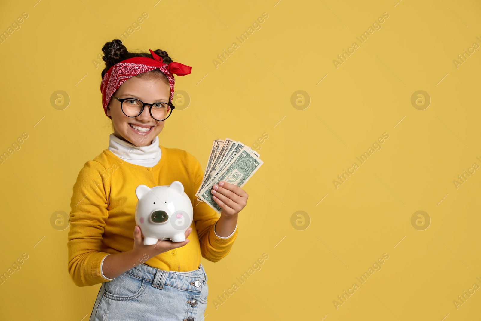 Photo of Pocket money. Cute girl with piggy bank and dollar banknotes on yellow background, space for text