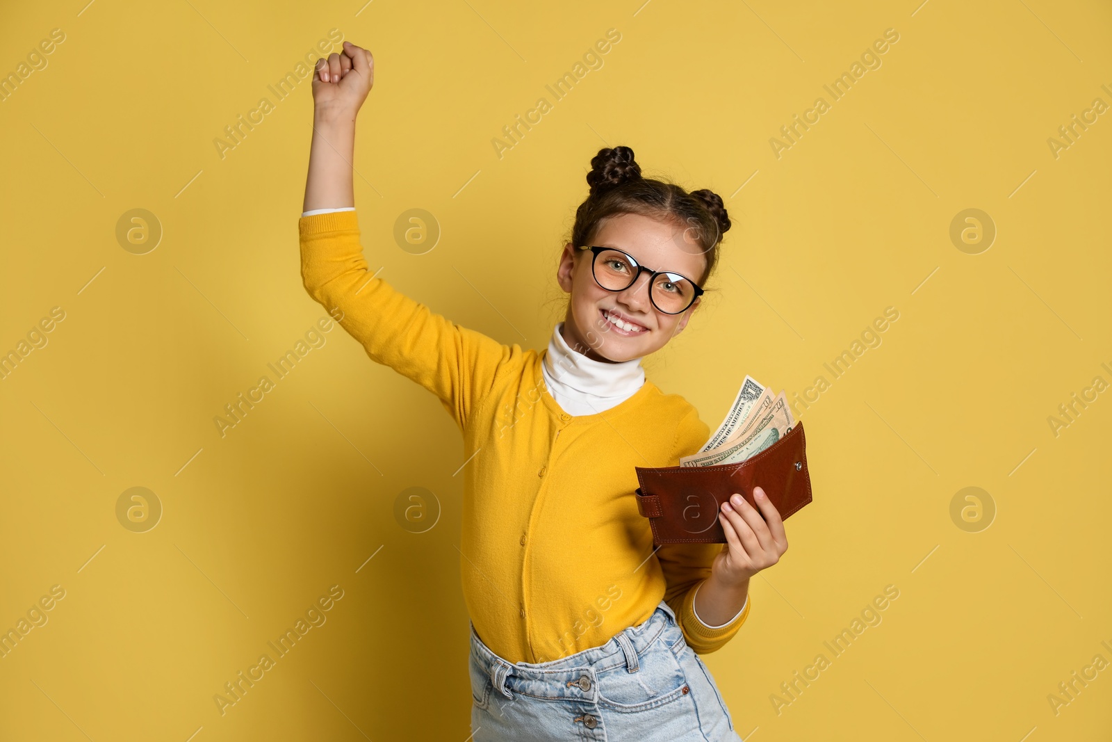 Photo of Pocket money. Cute girl with wallet and dollar banknotes on yellow background