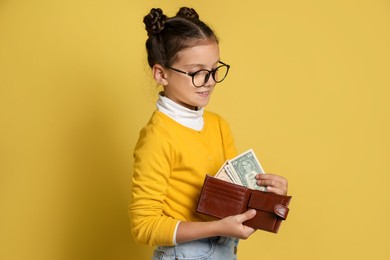 Photo of Pocket money. Cute girl with wallet and dollar banknotes on yellow background