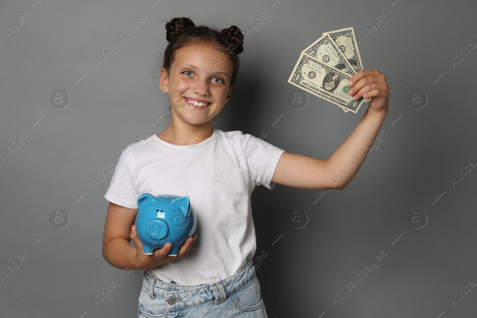 Photo of Pocket money. Cute girl with piggy bank and dollar banknotes on grey background