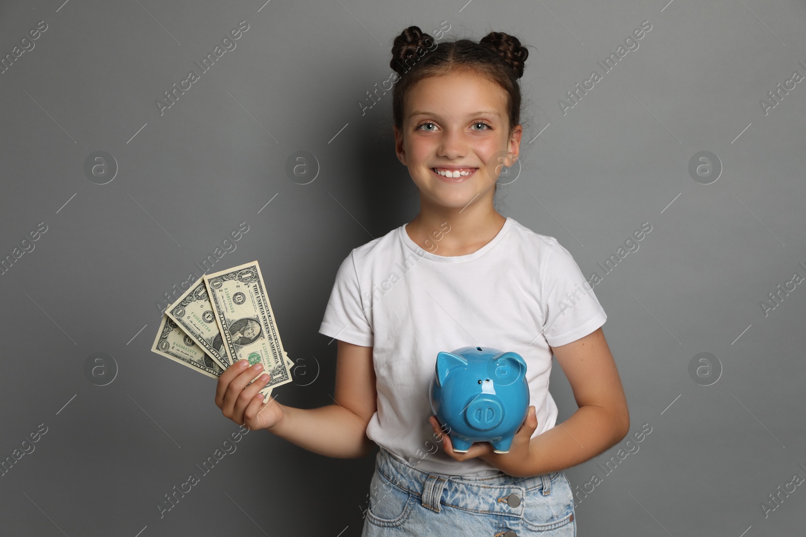 Photo of Pocket money. Cute girl with piggy bank and dollar banknotes on grey background