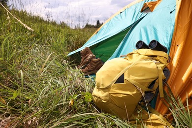 Tent, backpack, binoculars and shoes on green grass outdoors, space for text