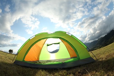 Photo of Tent on green grass in mountains, low angle view. Fisheye lens effect