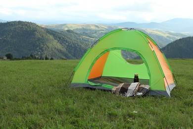 Photo of Tent, thermos and blanket on green grass in mountains, space for text