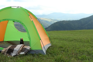 Photo of Tent, thermos and blanket on green grass in mountains, space for text