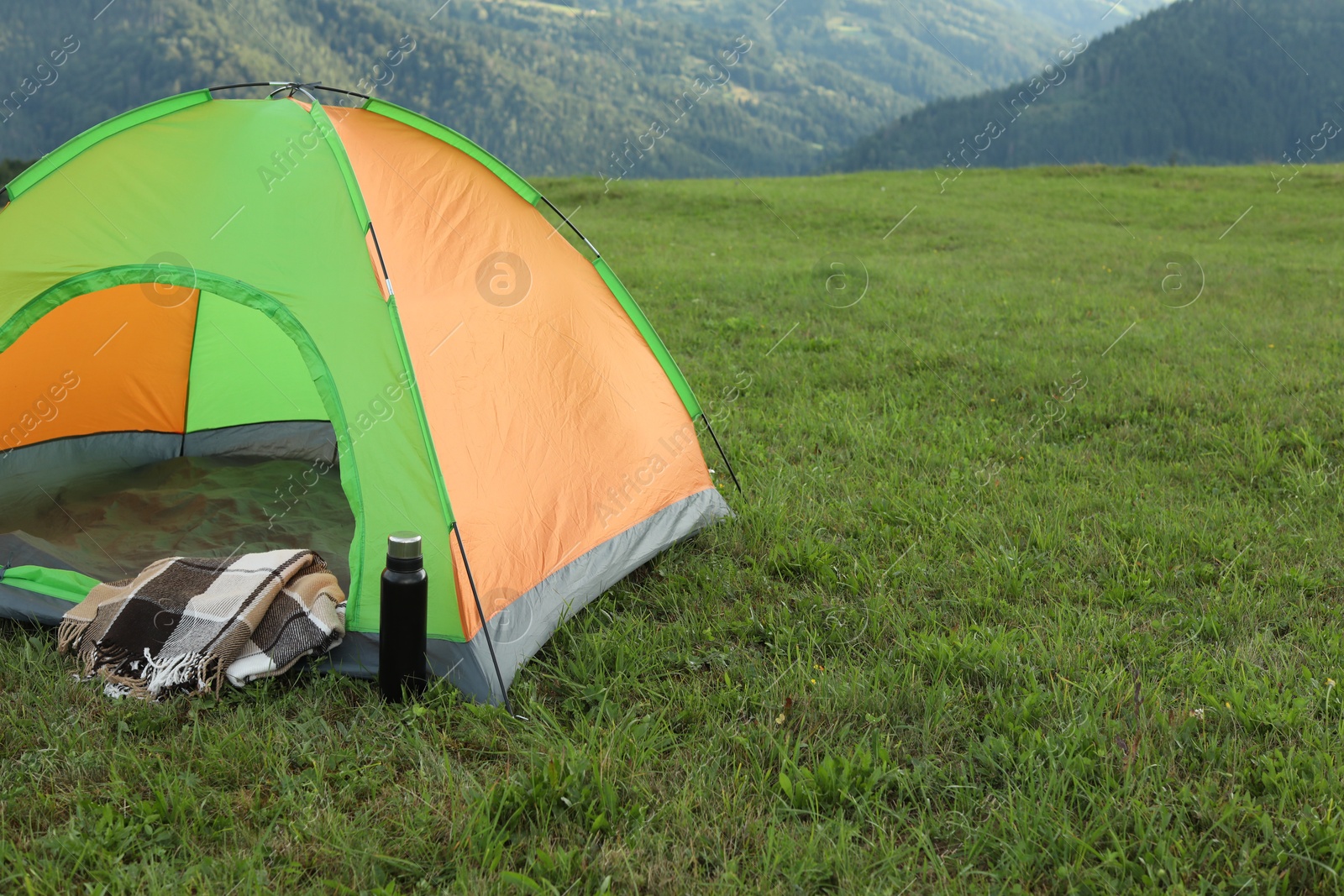 Photo of Tent, thermos and blanket on green grass in mountains, space for text