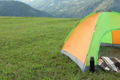 Tent, thermos and blanket on green grass in mountains, space for text